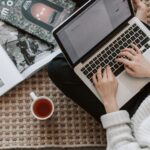 crop young businesswoman using laptop while drinking tea at home